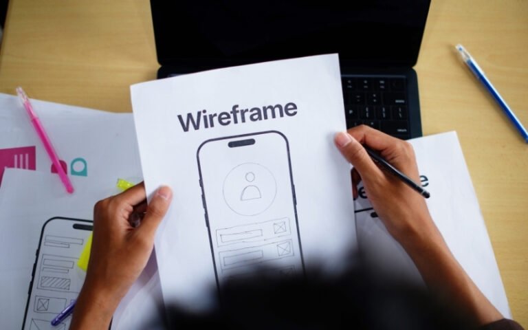 Designer sketching a mobile app wireframe by hand next to a laptop