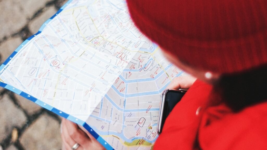 Person holding a folded street map and a phone while locating a place in a city