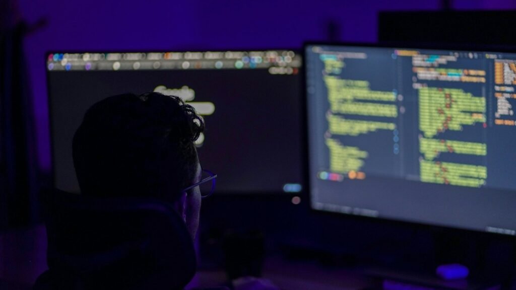 Developer reviewing code on two monitors in a darkened room
